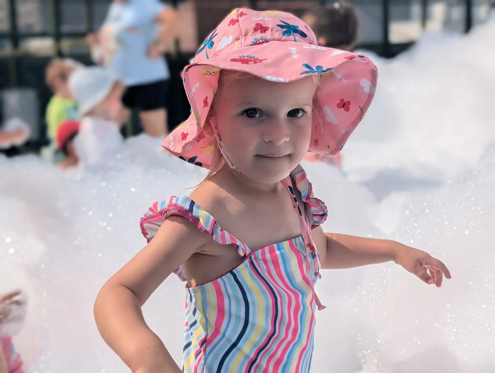 A child in a pink sunhat playing among bubbles